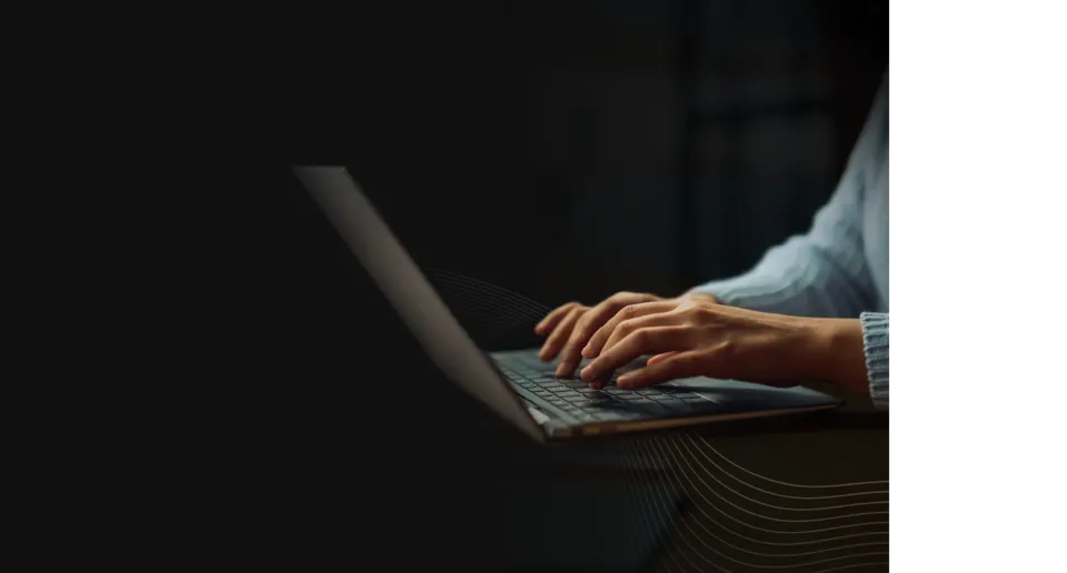 A close-up, atmospheric shot of a person's hands typing on a laptop keyboard in a dimly lit environment with subtle golden wave patterns overlaid in the corner.